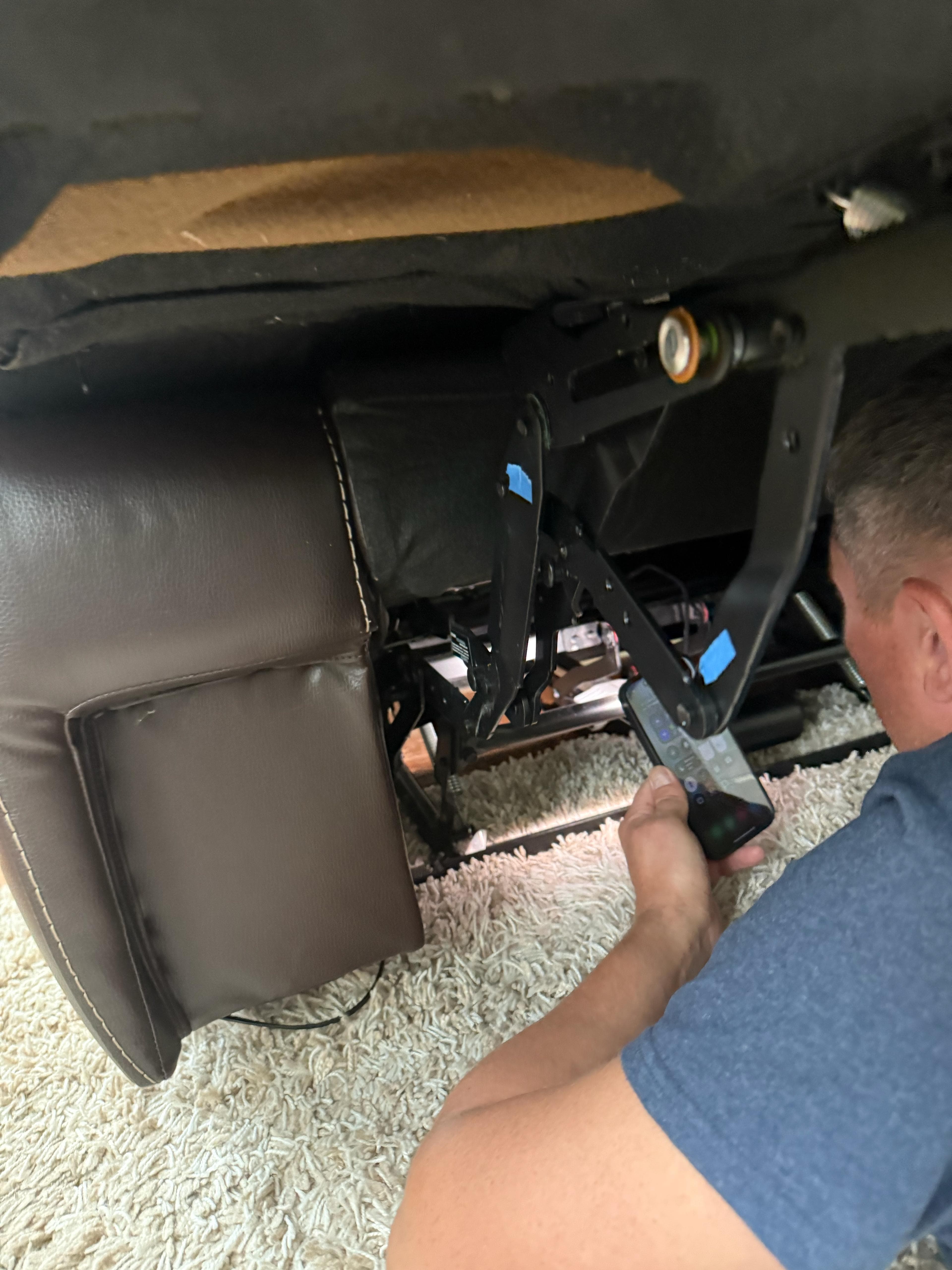 Technician inspecting an exposed power recliner mechanism in a customer home